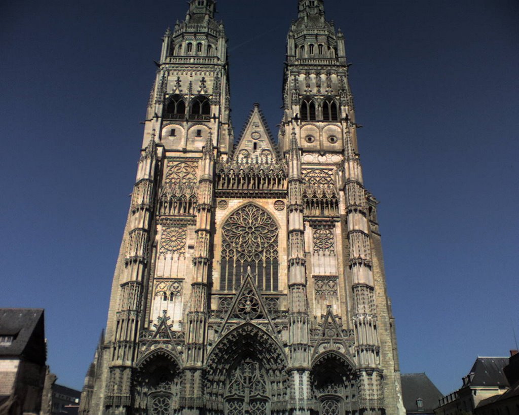 Façade de cathédrale gothique aux tours jumelles ornementées se découpant sur un ciel bleu clair, évoquant le patrimoine architectural de Tours
